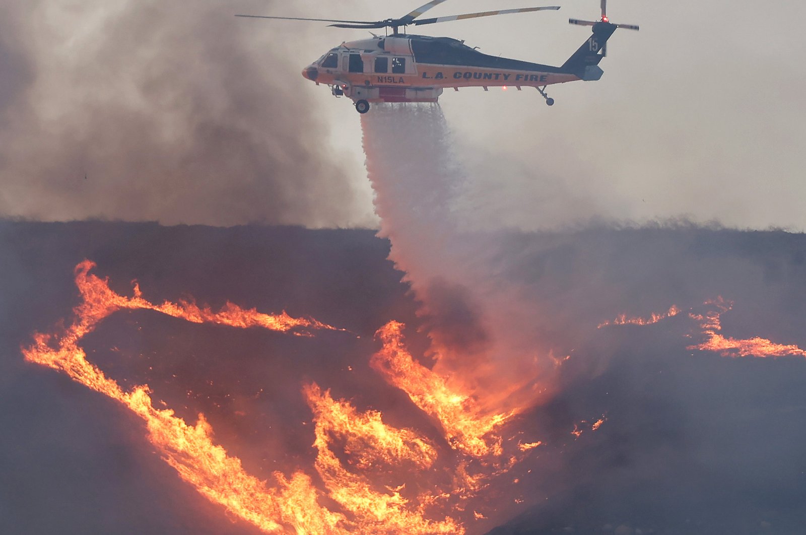 A firefighting helicopter drops water as the Hughes Fire burns north of Los Angeles near Castac, California on January 22, 2025.