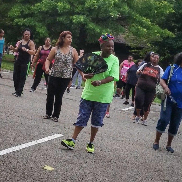 An old woman line dances in parking with other women