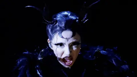 In the Eurovision last year, Reuters Bambi Thug was dressed in black, with black horns connected to his head. Her black hair is slippery and wearing white makeup on her face and black iilene.