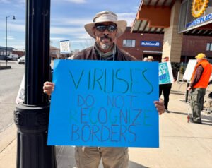 The person wearing a hat and sunshine has a blue bright sign that reads "The viruses do not recognize the borders."