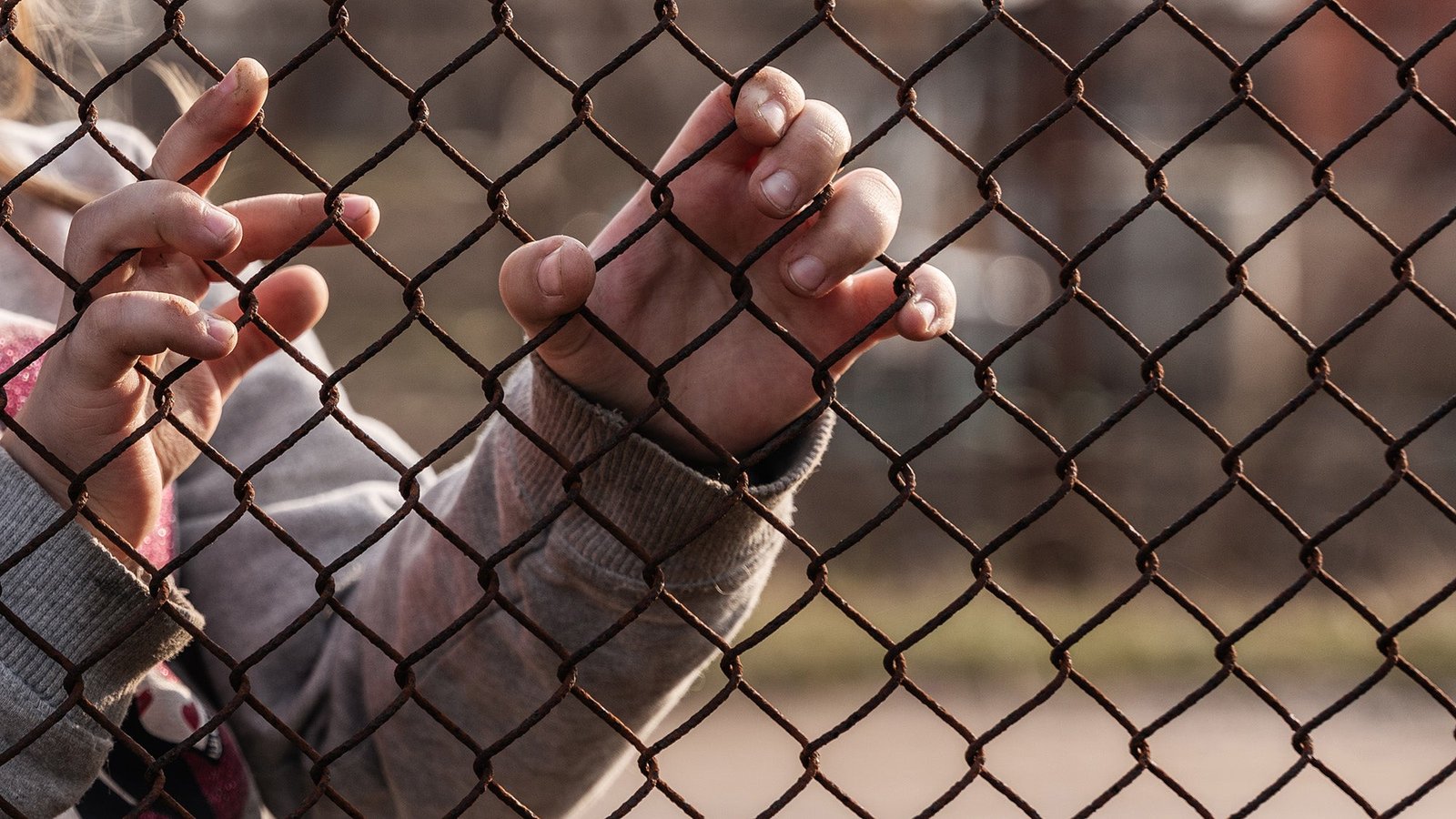 Child's hands holding onto a chain link fence.