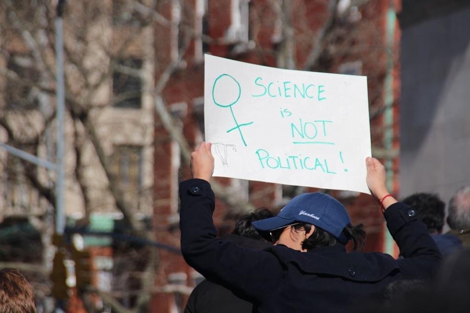 A person in the rally that has a symbol that & quot; Science is not political! & quot; With a female symbol