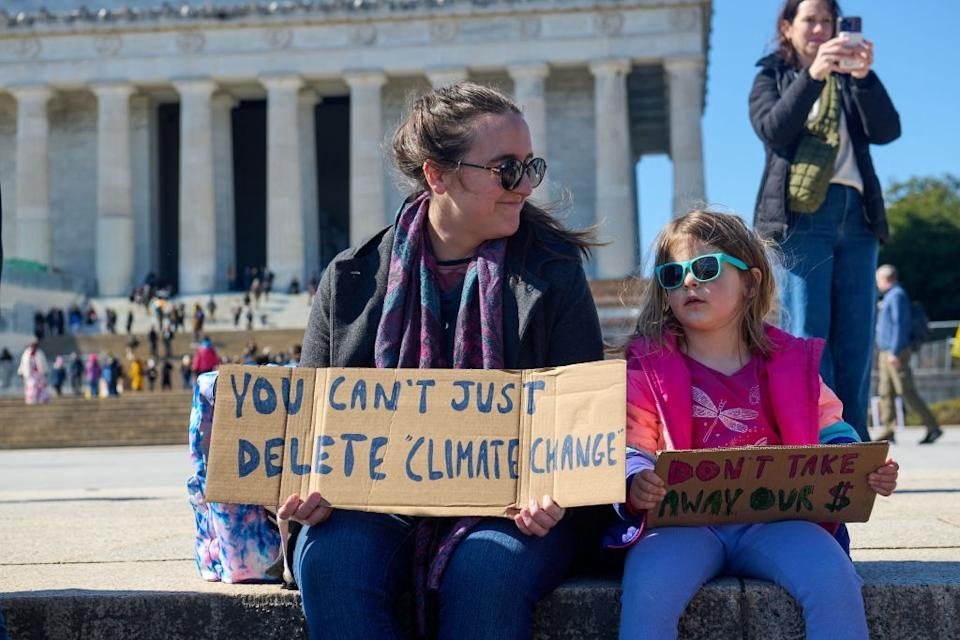 An adult and child with protests about climate change in front of the historic building sitting while sitting while sitting.