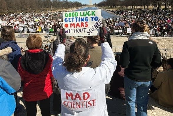 A crowd gathers out with a person with a sign: & quot; Good luck going to Mars without science, & quot; A & quot; Crazy scientist & quot; Lab coat