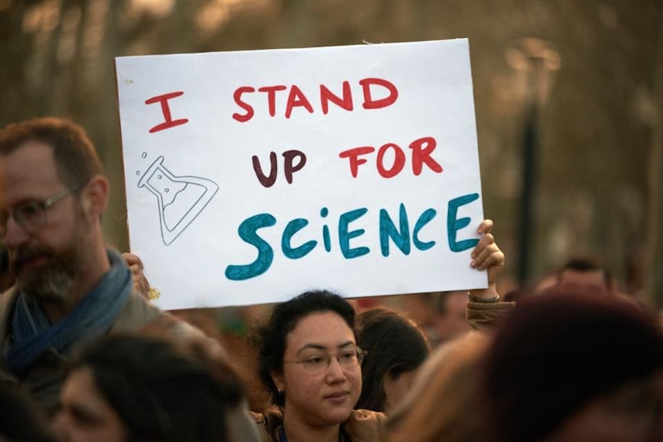 The person has a symbol that reads & quot; I stand for science & quot; With a Baker drawing, in a demonstration between the crowd