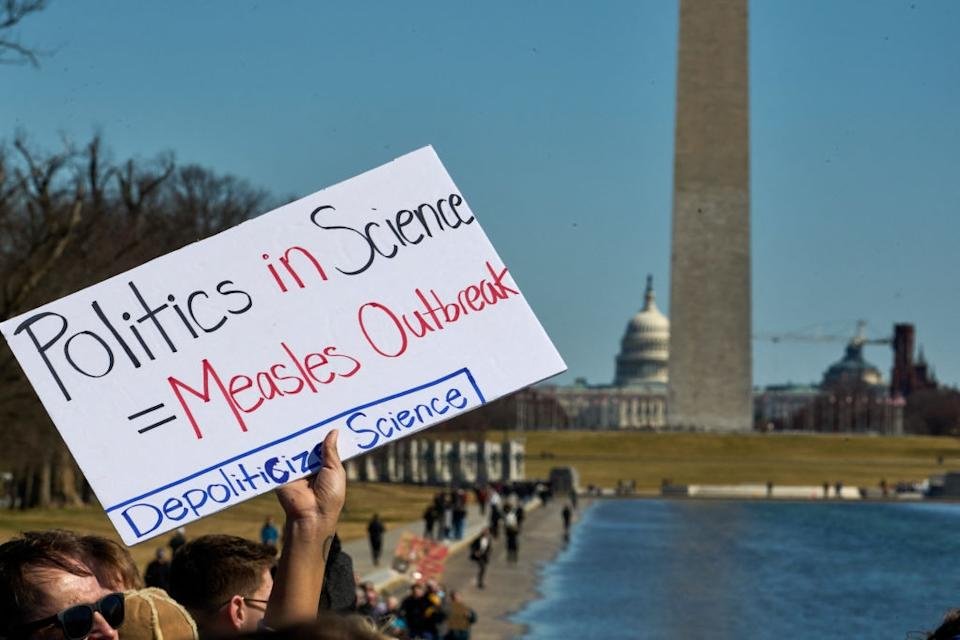 The person holds a sign near the Washington monument that reads, & quot; Politics in politics = spreading measles, eliminating science. & quot;