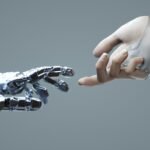 Digital image of a robotic and a human hand touching a finger against a grey backdrop.