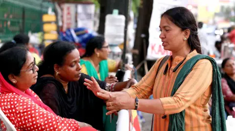 Vivek R Nair/BBC is a protest coordinator, Sabora Arifa, seen in yellow karta and green dupatta, standing across two protest volunteers - in a red, one in a dark color. 