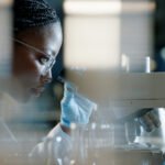 Scientist, microscope and analysis in lab for healthcare, innovation and development in stem cell research. Black woman, investigation and experiment with biotech for dna, exam or test for bacteria